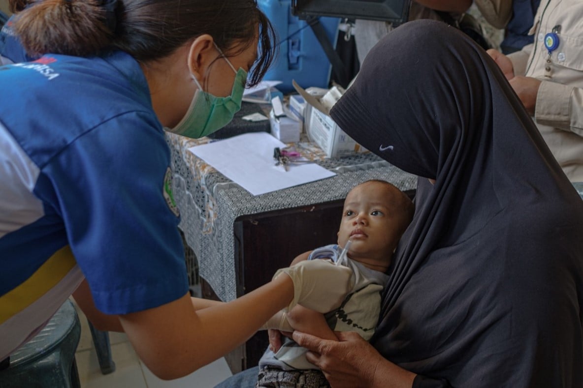 A health worker preparing to vaccinate a baby, who is on his grandmother's lap.